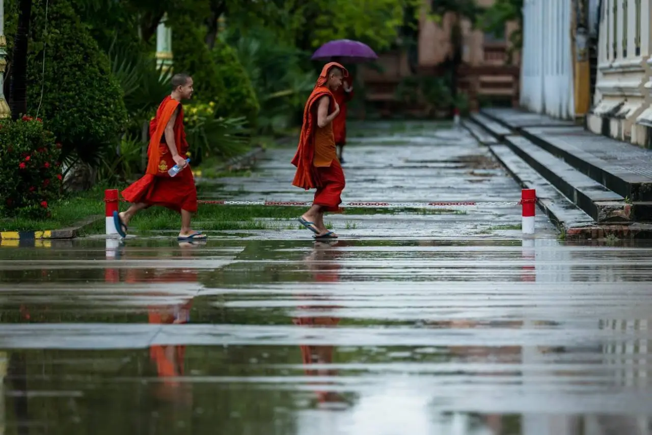 Two monks with an umbrella walk on a rainy street in Battambang, Cambodia.