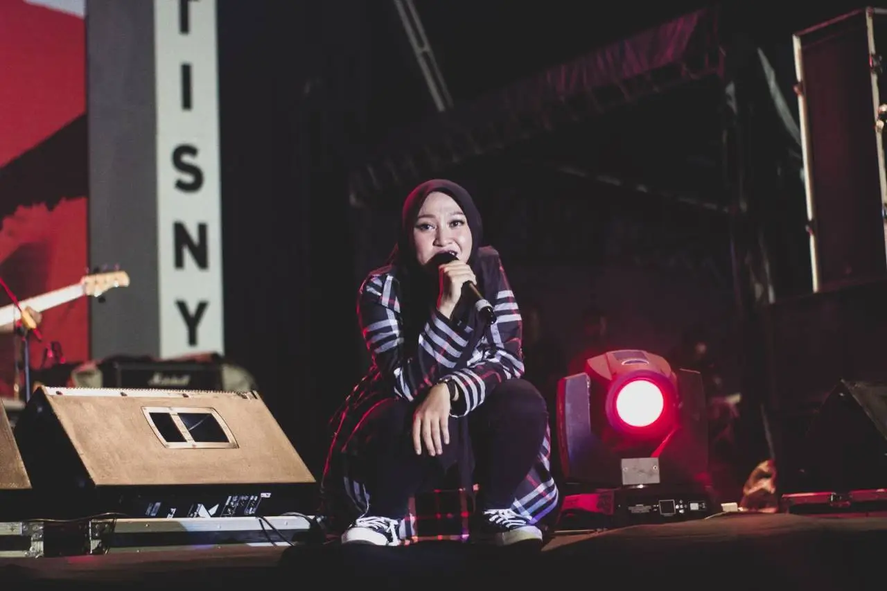 A female singer in a hijab performing on stage during a night concert in Sibolga, Indonesia.